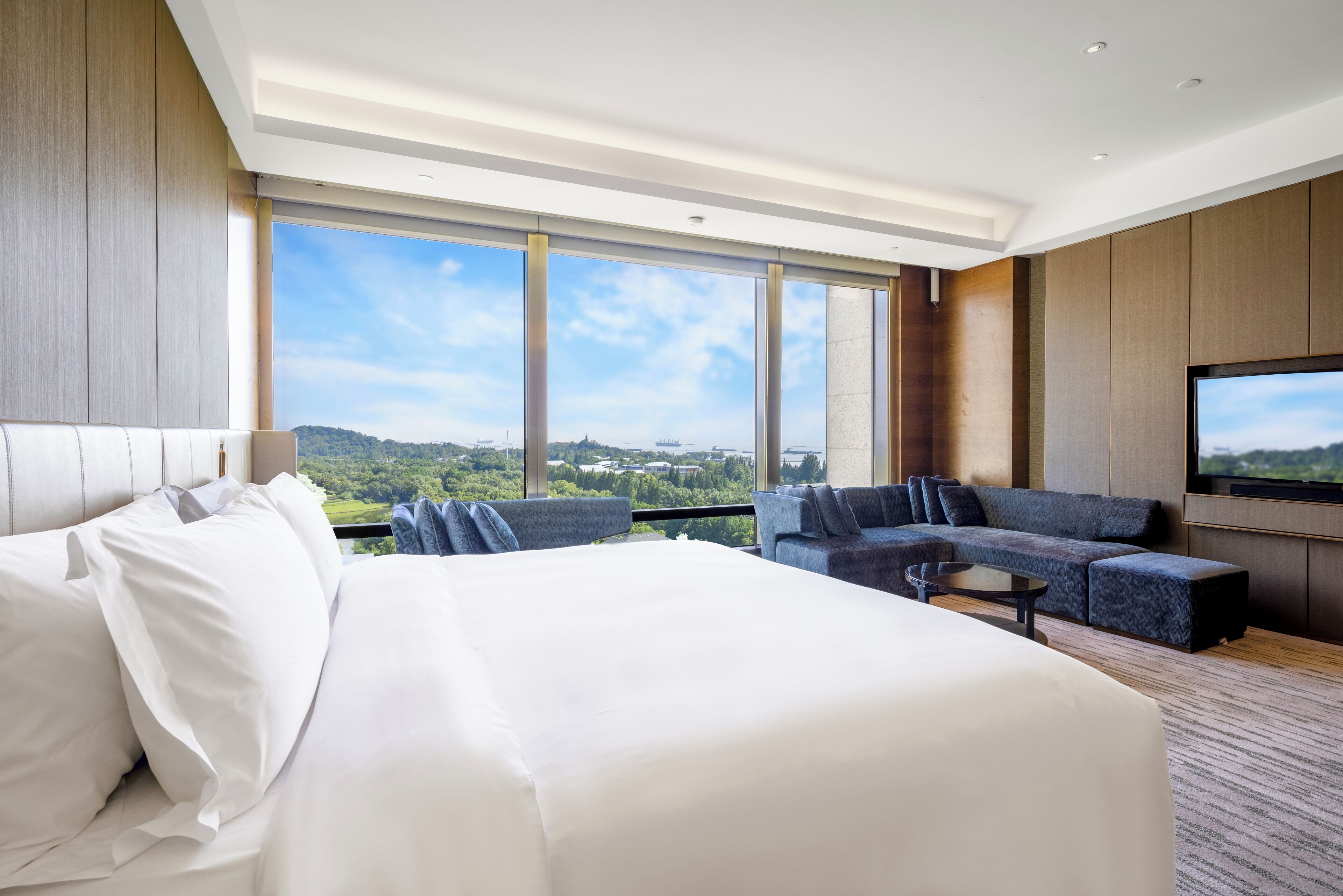 A modern hotel room with a large bed, a sofa, a coffee table, and a TV.