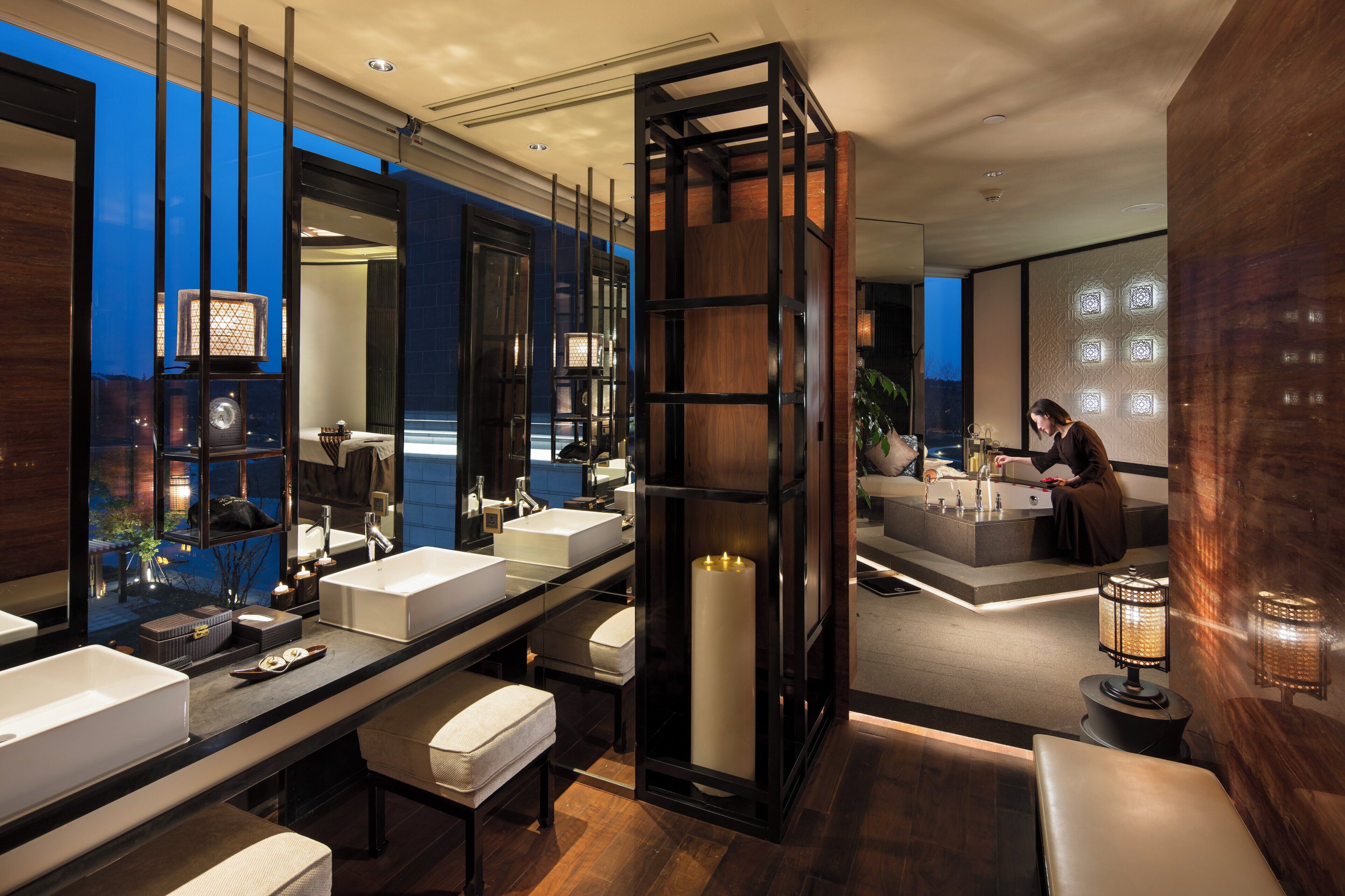 A modern bathroom with a large mirror, two sinks, a bathtub, and a bench.