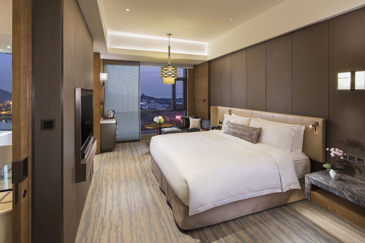 Een moderne hotelkamer met een groot bed, een bureau en uitzicht op de stad in de schemering.