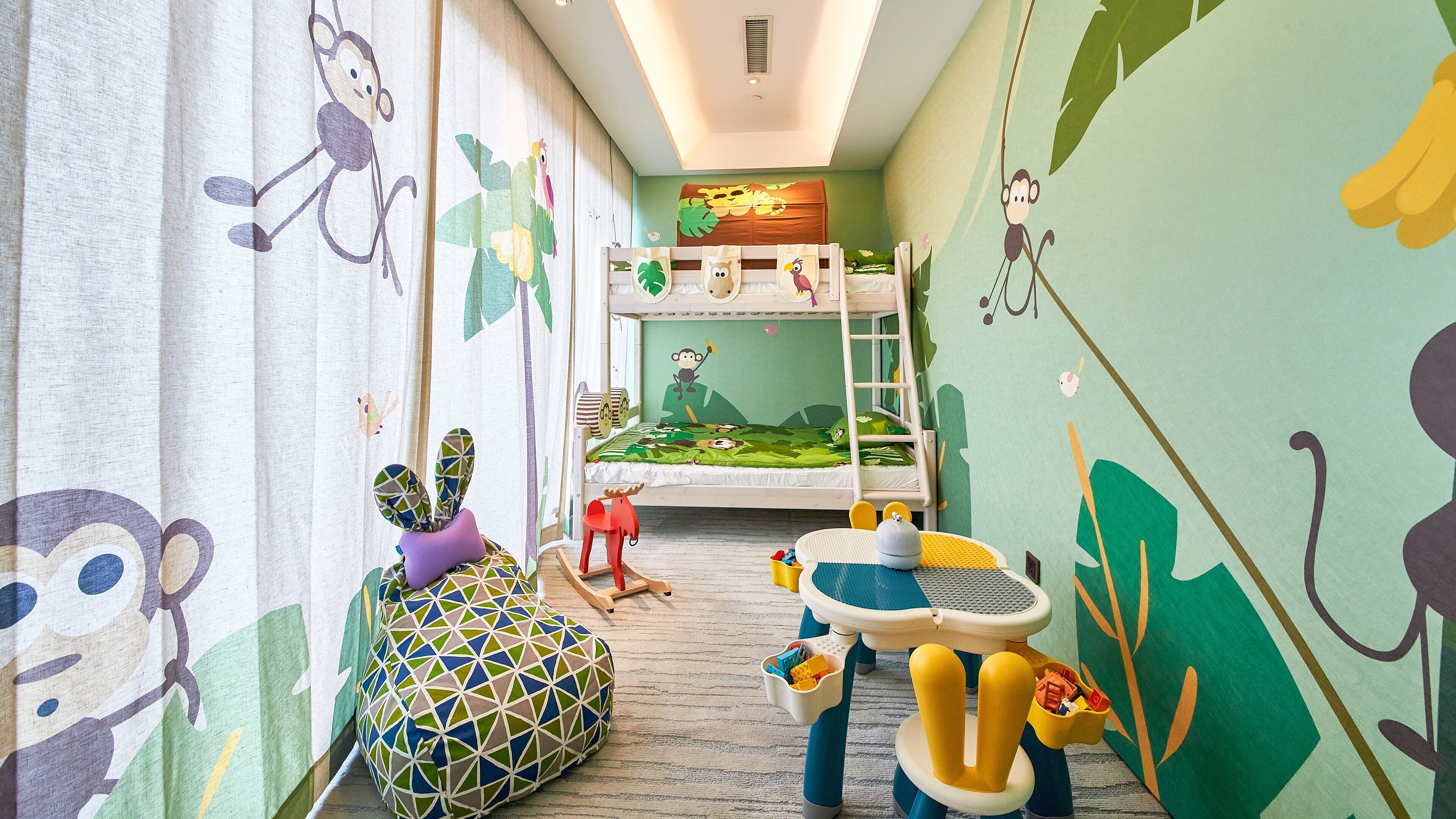 A child's bedroom with a bunk bed, a play area with toys, and a window with curtains.