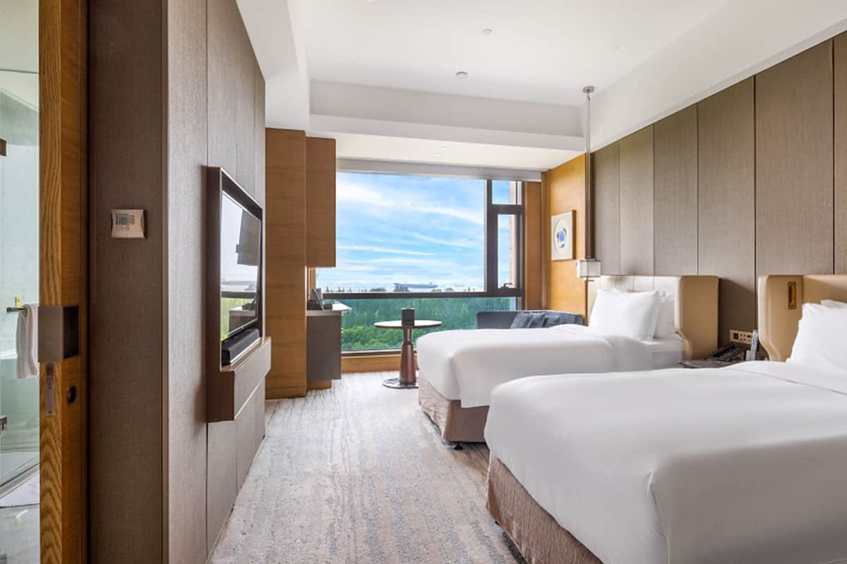 Een hotelkamer met twee bedden, een televisie, een tafeltje en uitzicht op het omliggende landschap.