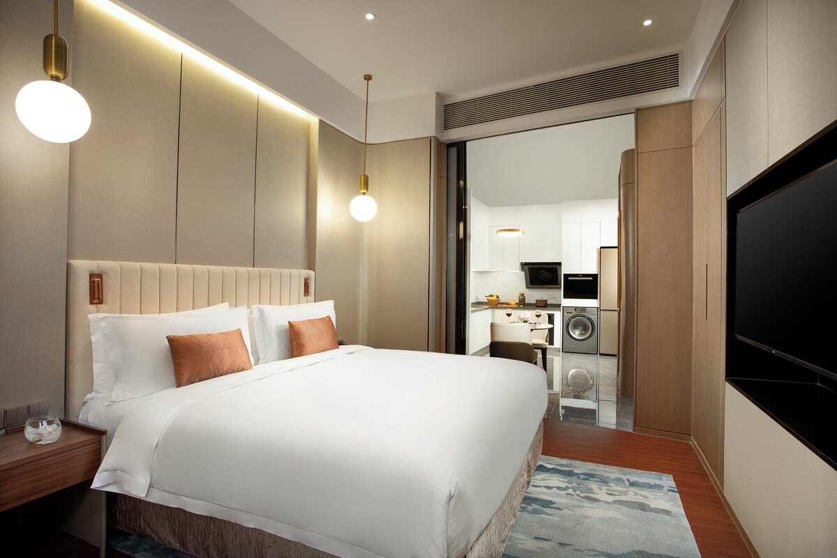A hotel room with a bed, bedside tables, a TV, a bathroom, and a kitchenette.