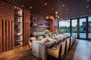 Un restaurante con una larga mesa de comedor preparada para una comida, paredes de madera y vistas amplias a través de grandes ventanales.
