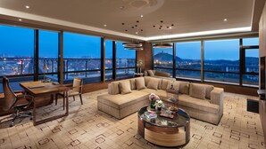 A spacious living room with a large sofa, a coffee table, and a desk with a chair. The room has large windows offering a city view. - InterContinental Nantong by IHG (Nantong)