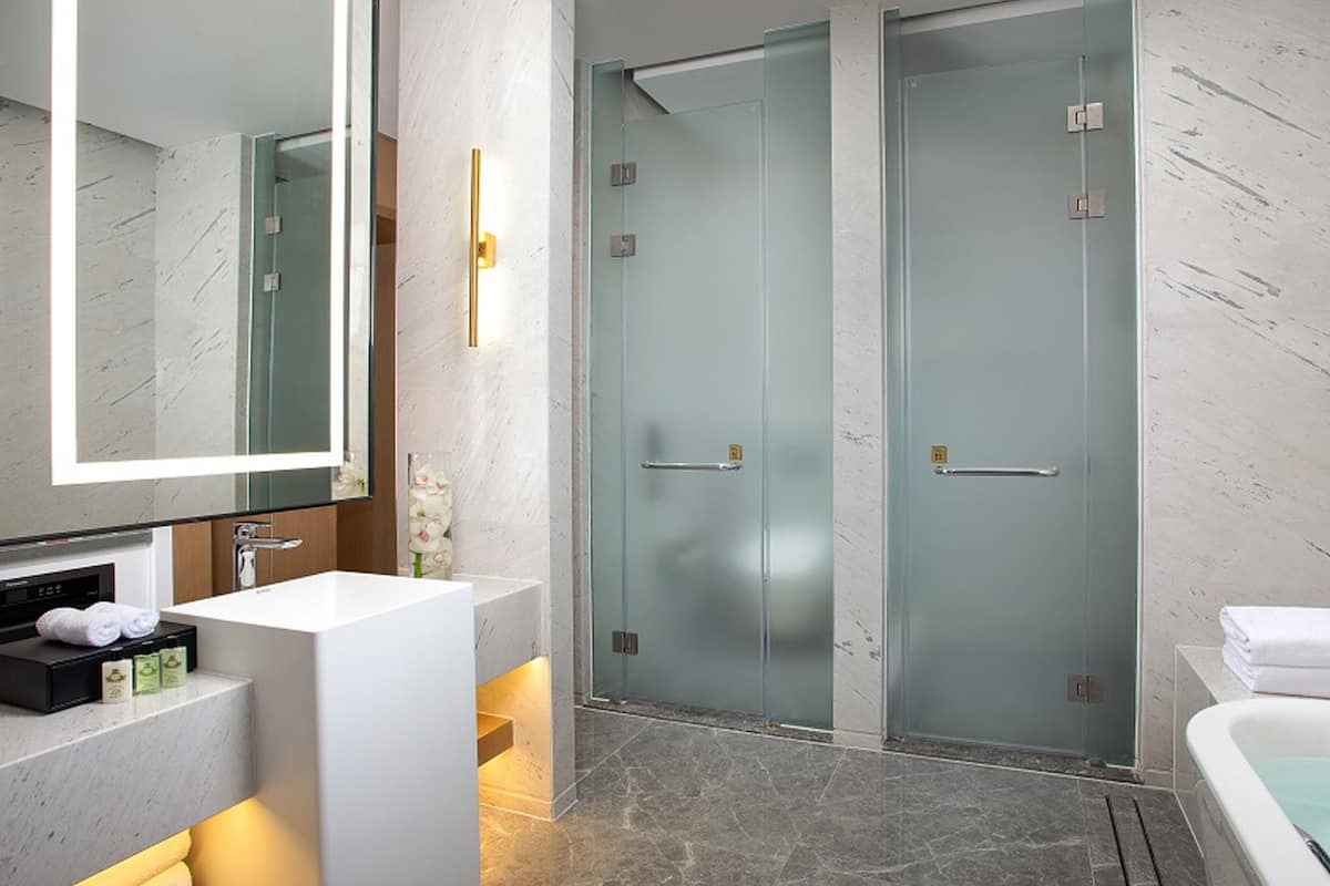 Een moderne badkamer met een witte wastafel, een grote spiegel, een douche met glazen wanden en een bad.