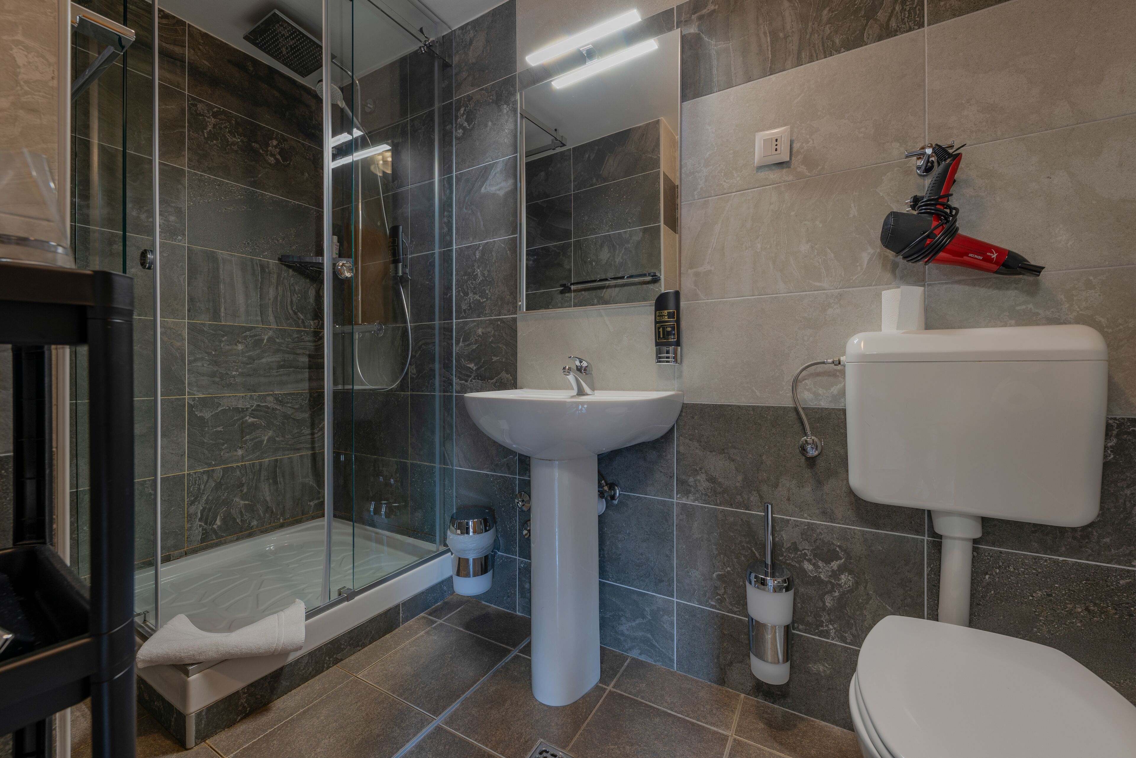 A modern bathroom with a glass shower enclosure, a pedestal sink, and a toilet.