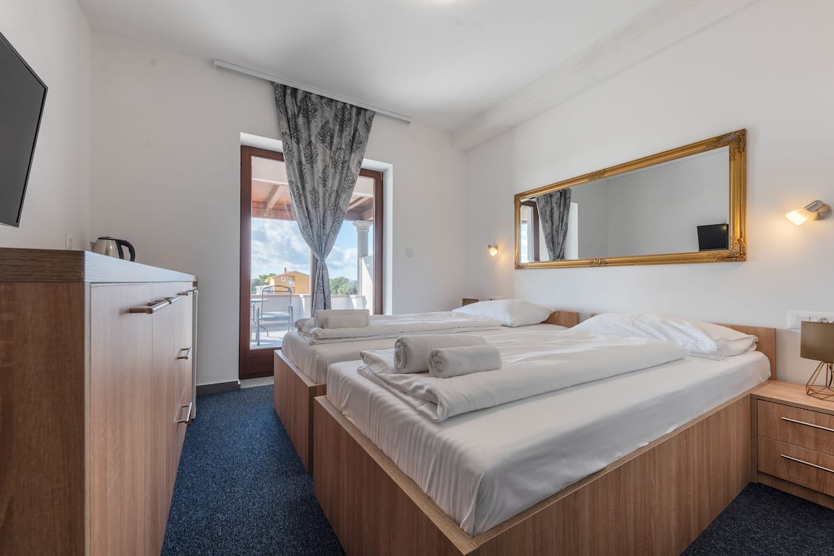 A hotel room with two beds, a wooden wardrobe, a mirror, and a window with curtains.
