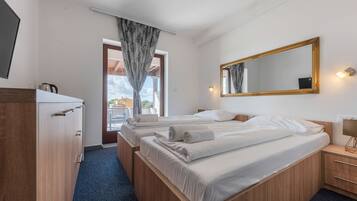 A hotel room with two beds, a wooden wardrobe, a mirror, and a window with curtains.