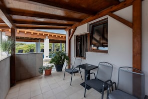 Um alpendre coberto com chão de azulejos, mesa com cadeiras e plantas em vasos.