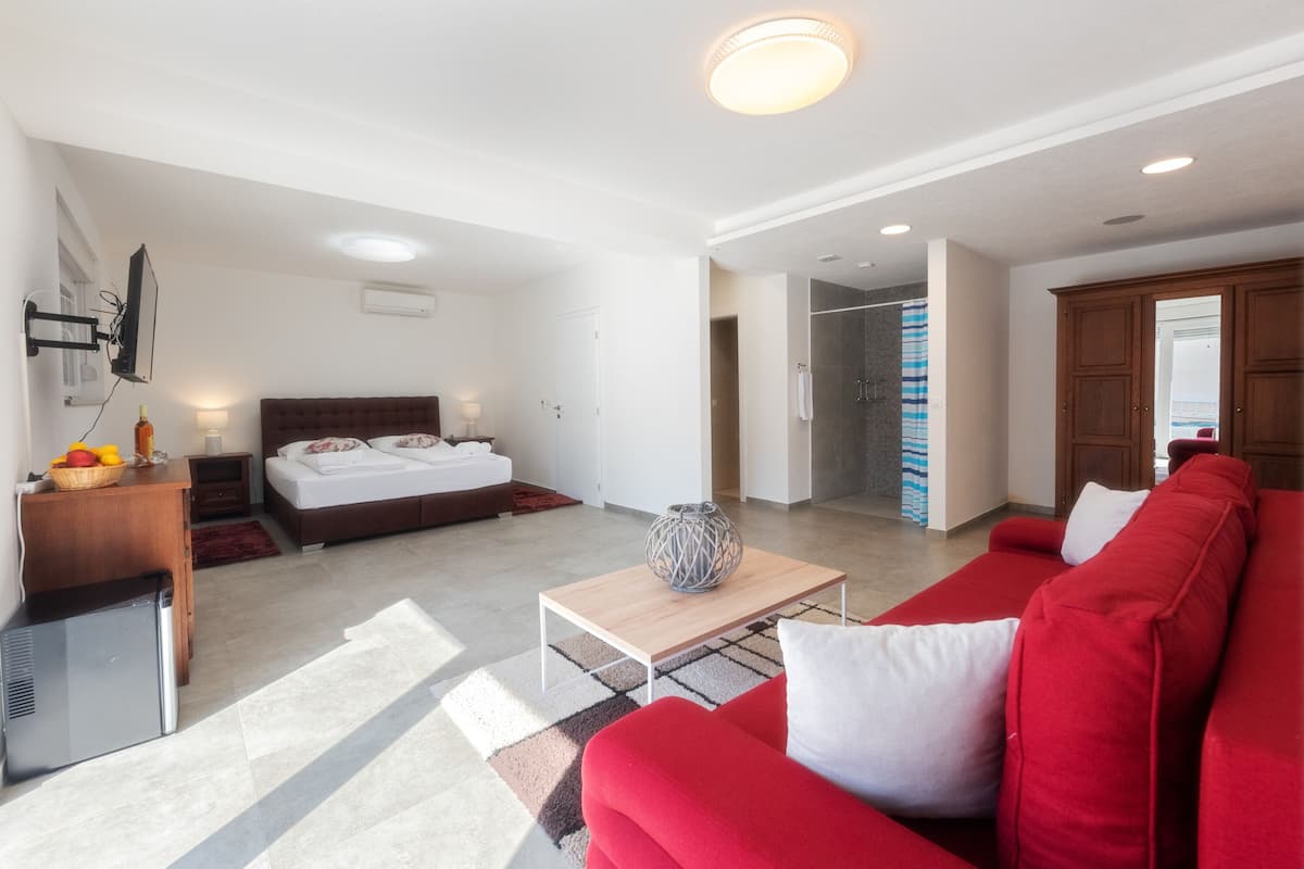 A modern hotel room with a bed, a red sofa, a small table, and a TV.