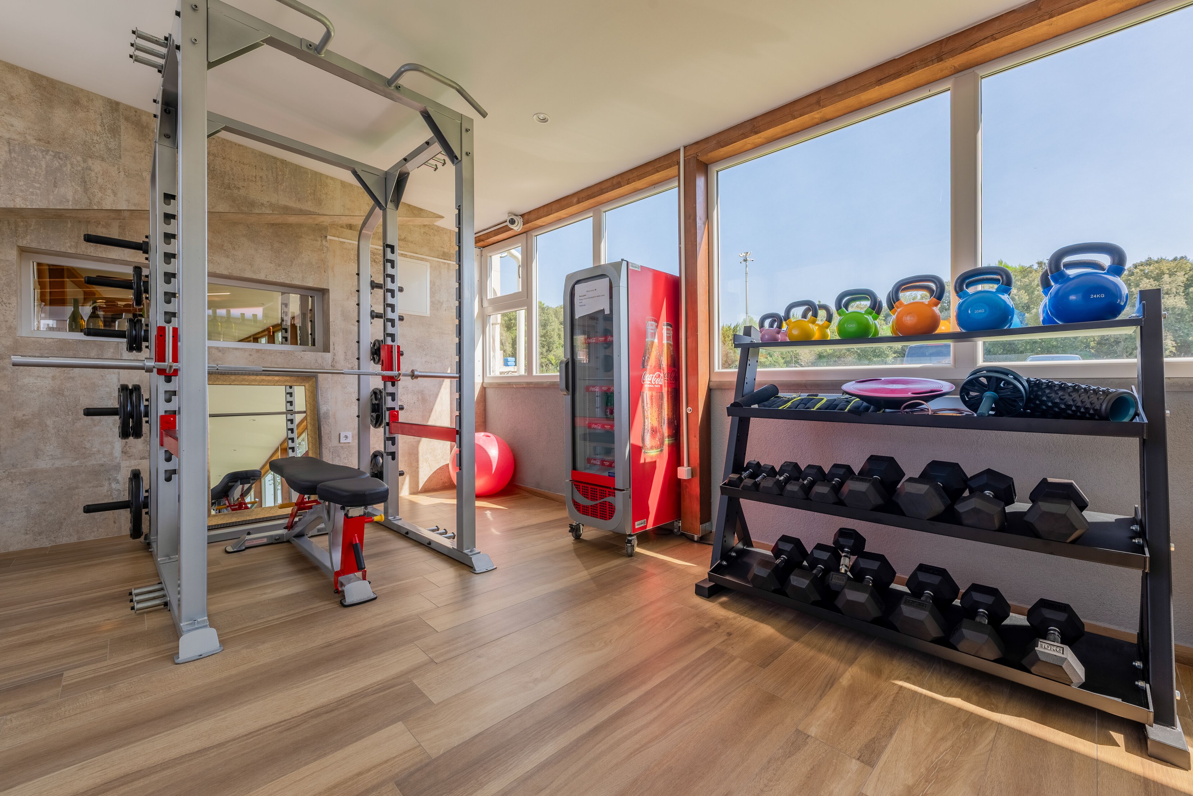 A gym with a weight bench, squat rack, kettlebells, and dumbbells.