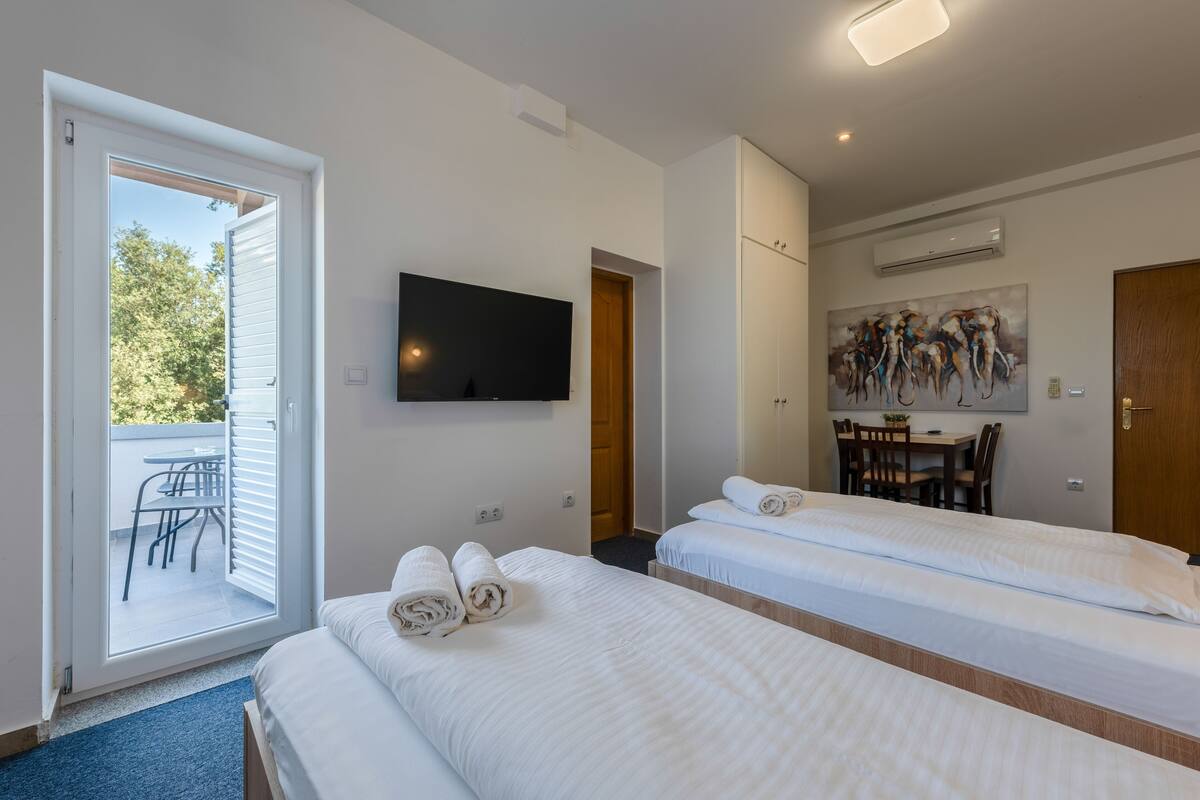 A hotel room with two beds, a TV, a painting, and a balcony.