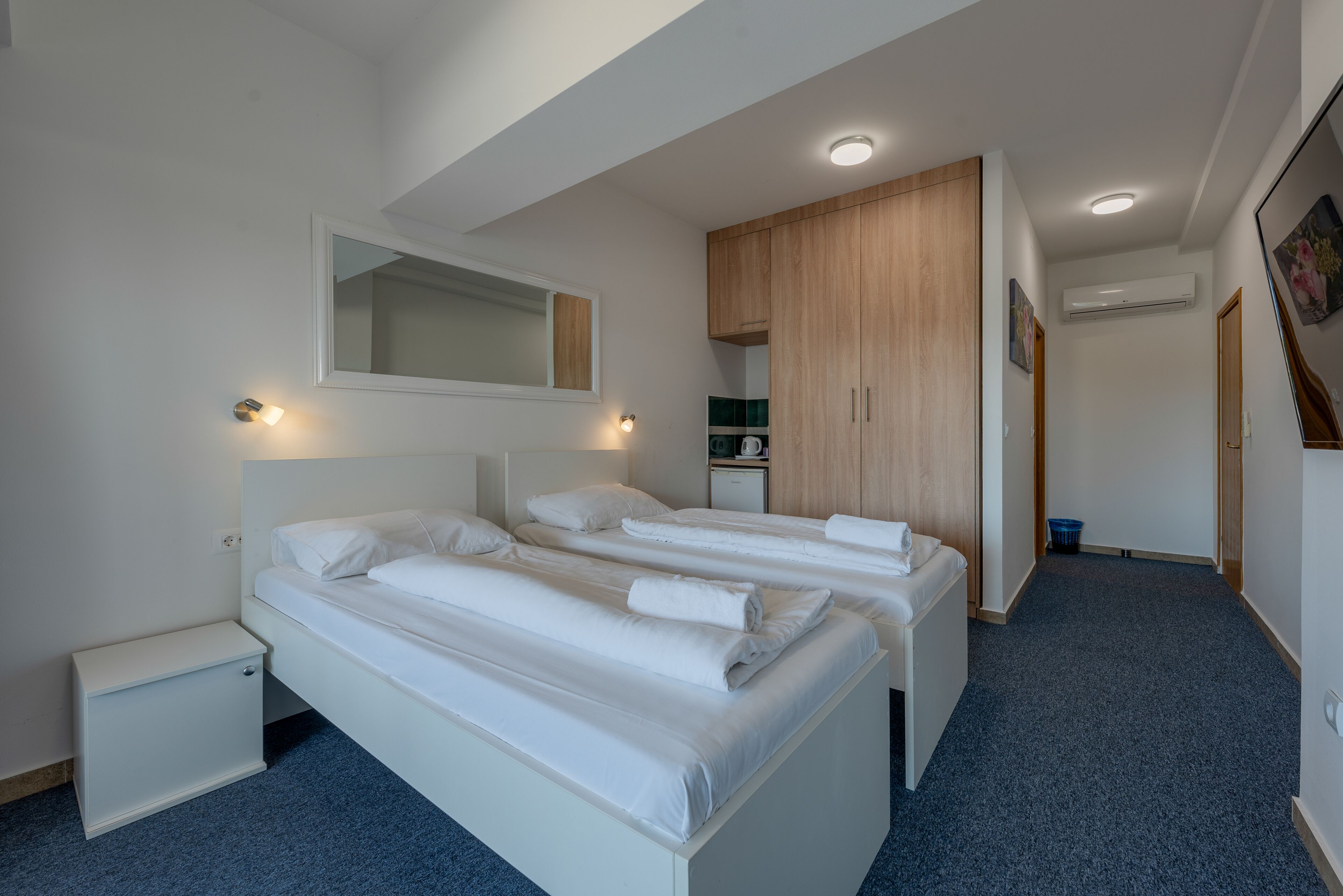 Habitación de hotel con dos camas, una mesita de noche pequeña, un espejo y un armario.