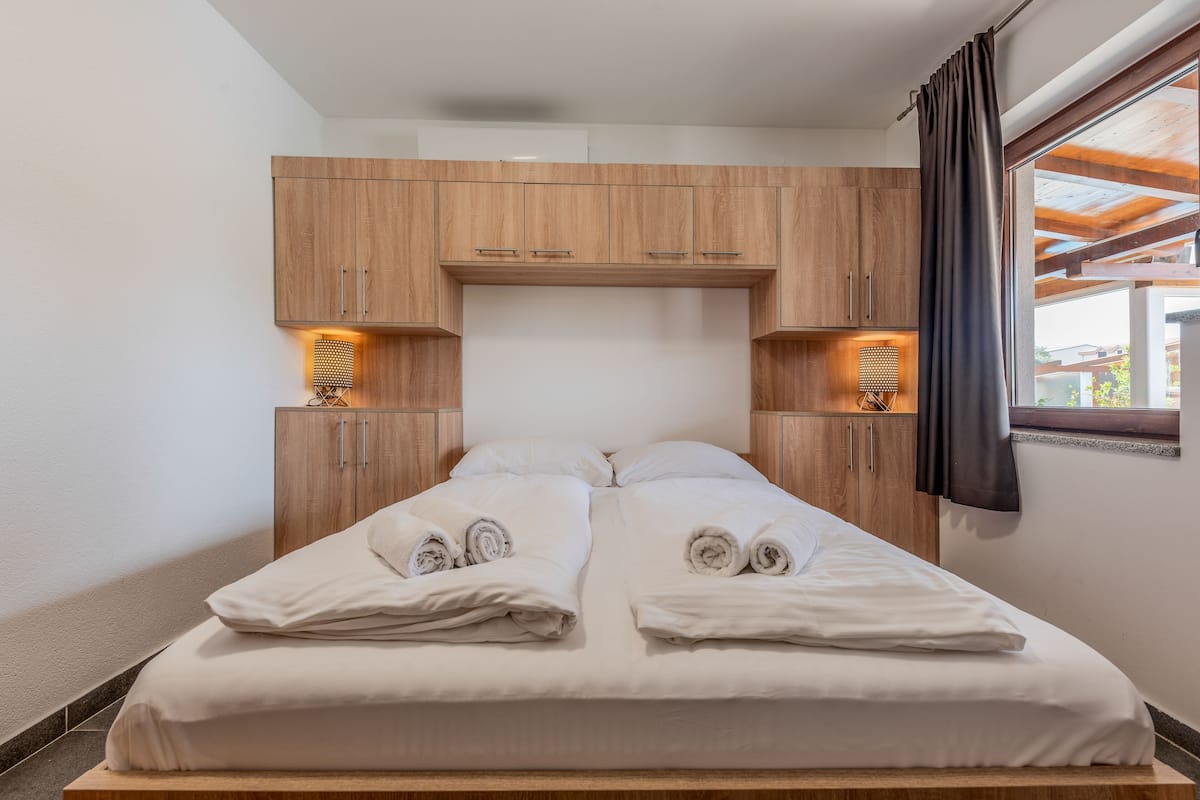 A double bed with white linens and towels, wooden headboard cabinets, and two wall-mounted lamps.