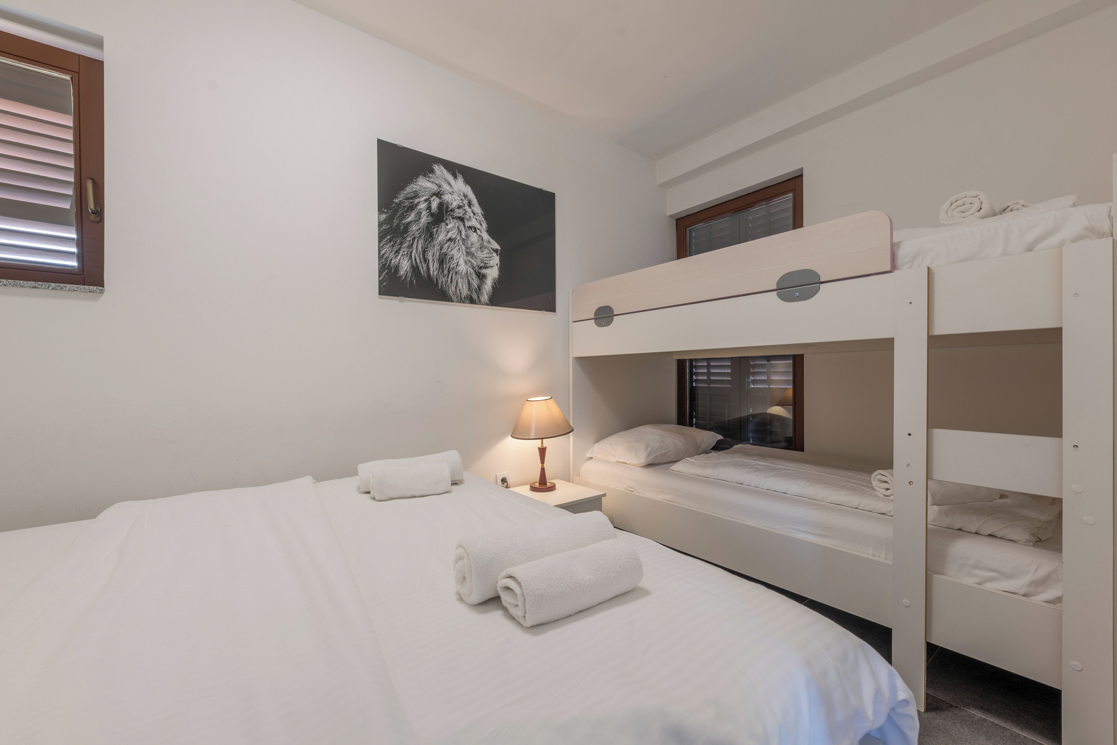 Une chambre d’hôtel avec un lit superposé, un lit simple, une lampe fixée au mur et un tableau encadré.