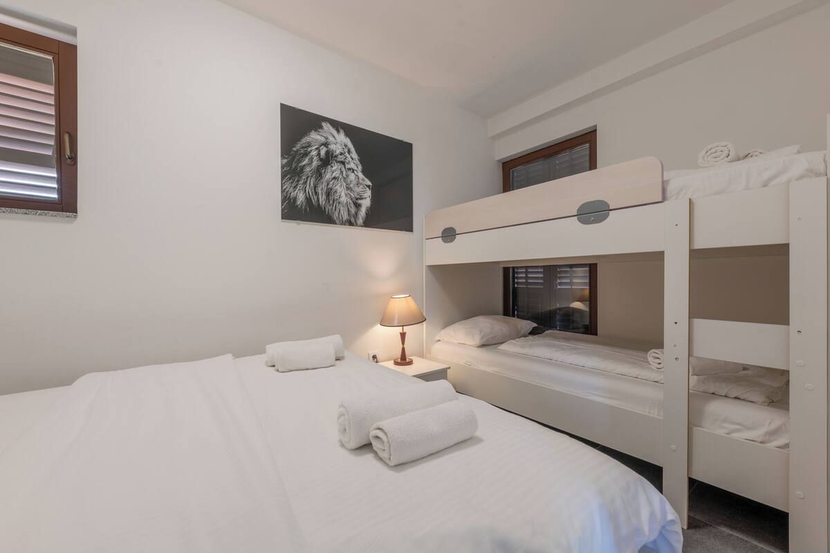 A hotel room with a bunk bed, a single bed, a wall-mounted lamp, and a framed picture.