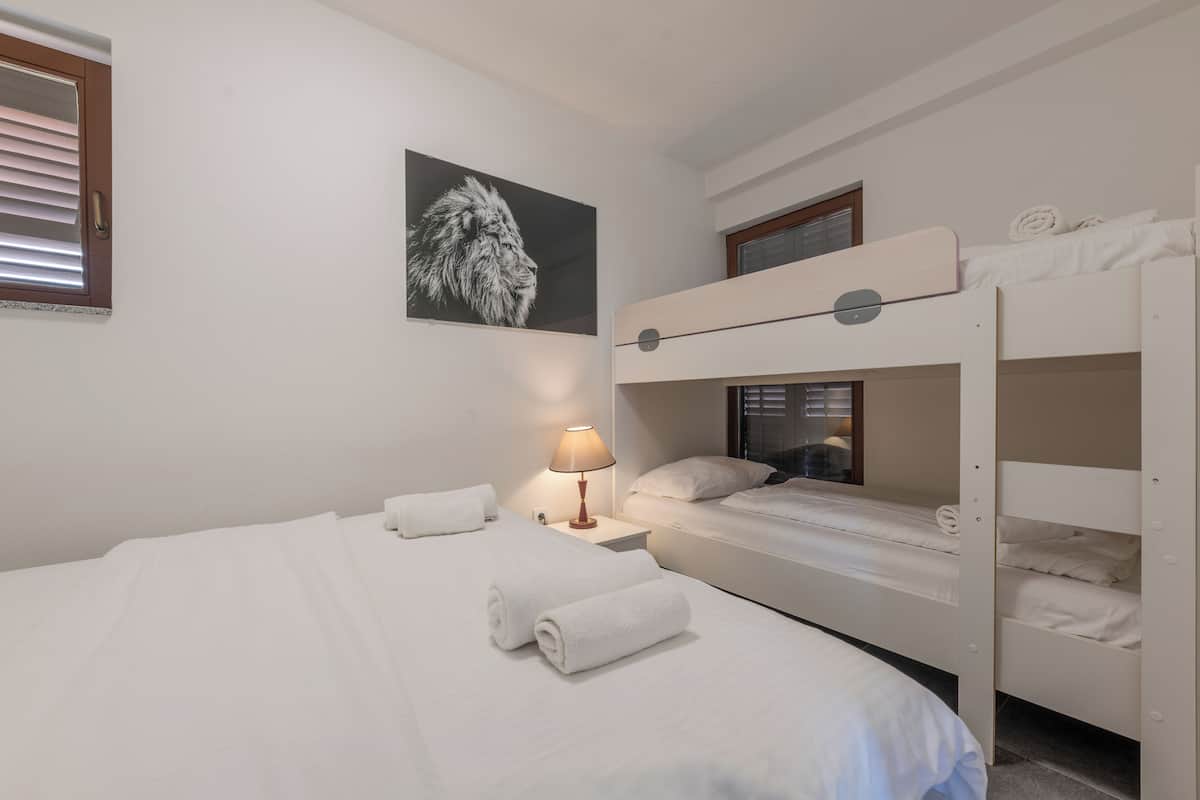 Une chambre d’hôtel avec un lit superposé, un lit simple, une lampe fixée au mur et un tableau encadré.