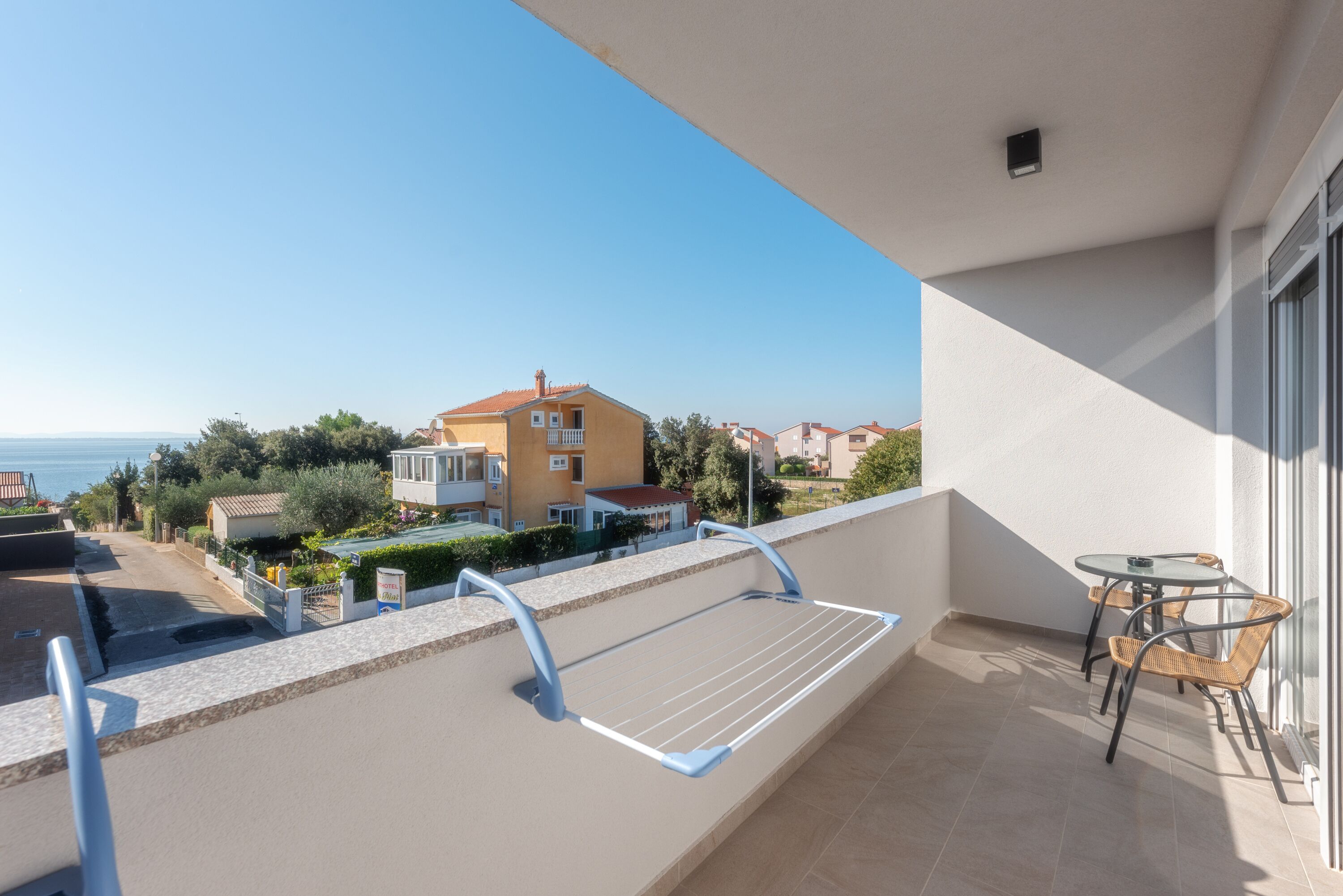 A balcony with a view of a yellow building and the sea.