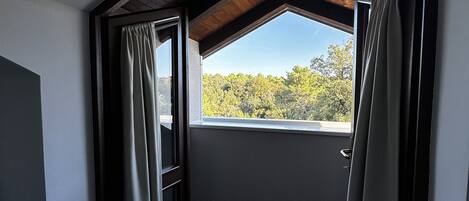 A room with a sloped ceiling, a large window with curtains, and a view of trees outside.