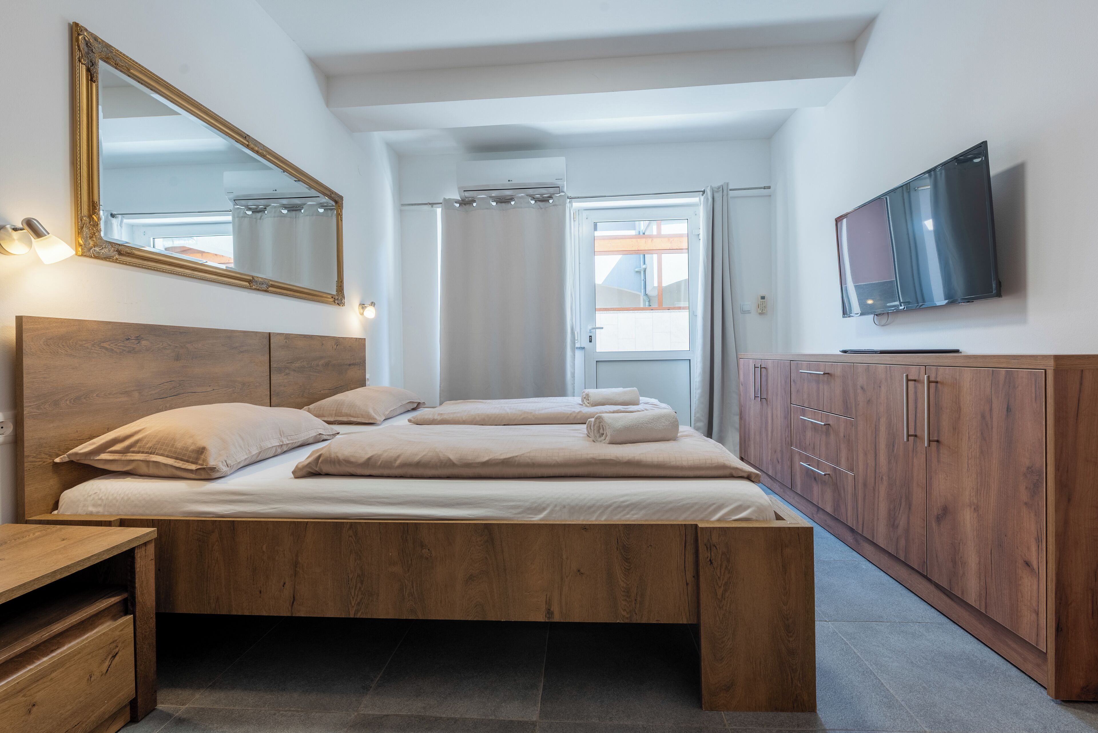 Une chambre à coucher avec un lit en bois, un grand miroir, une télévision et une armoire.