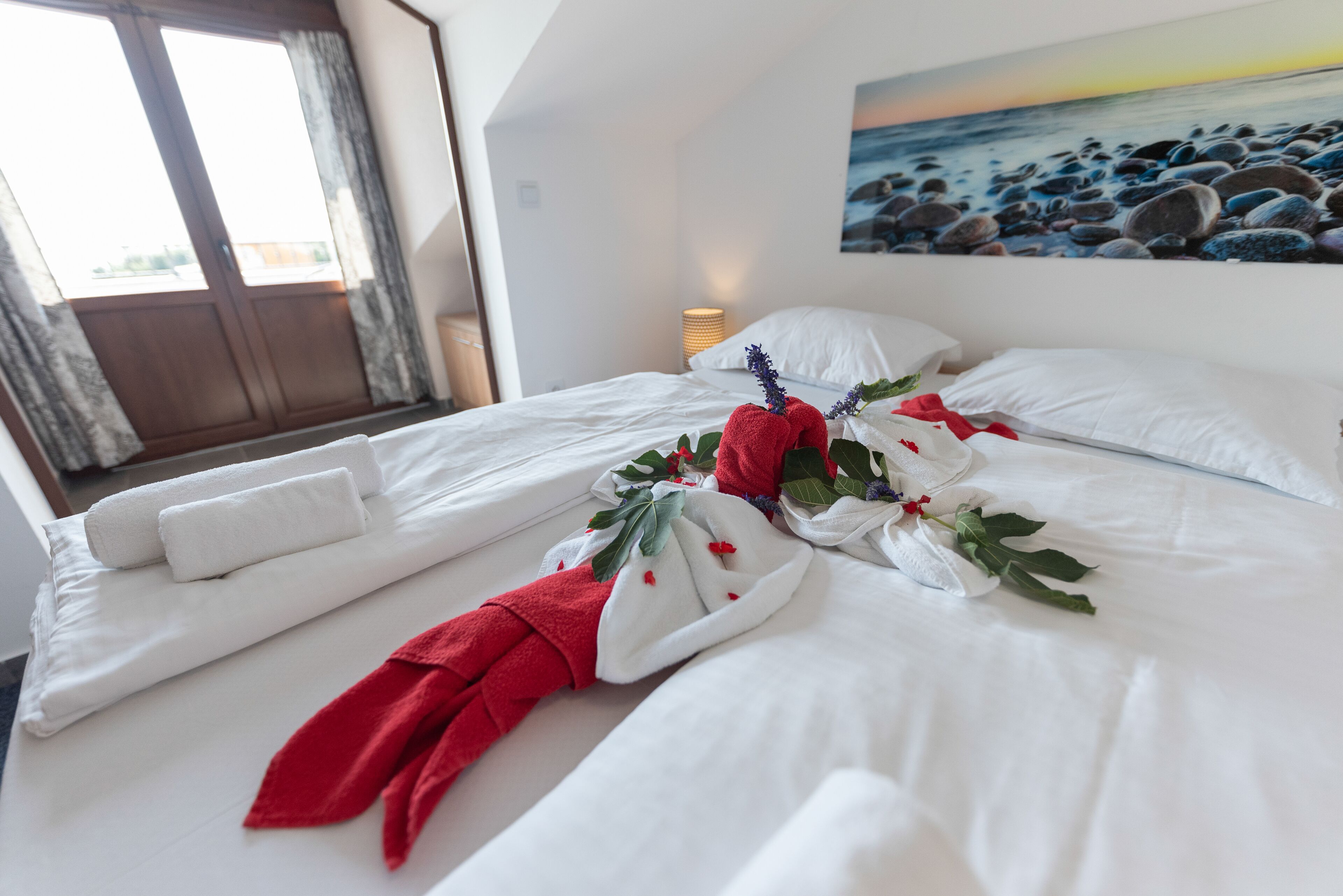 Una cama bien hecha con sábanas blancas, toallas rojas y un arreglo floral.