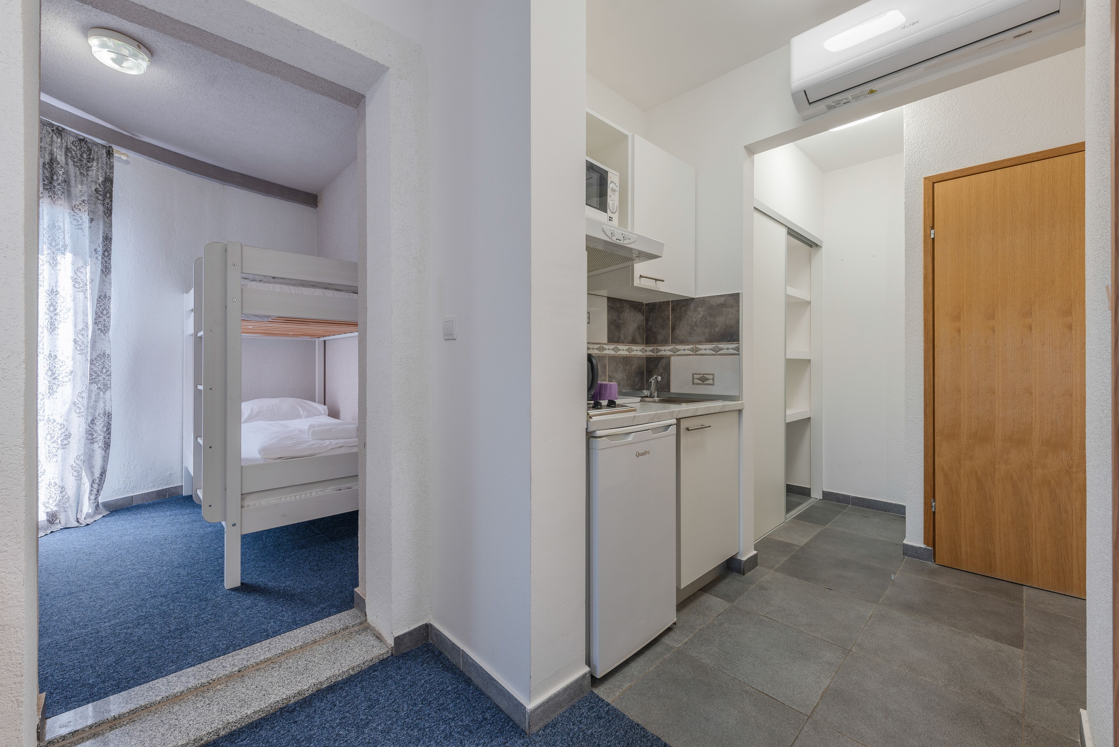 Una habitación pequeña con literas, un kitchenette y una puerta de madera.