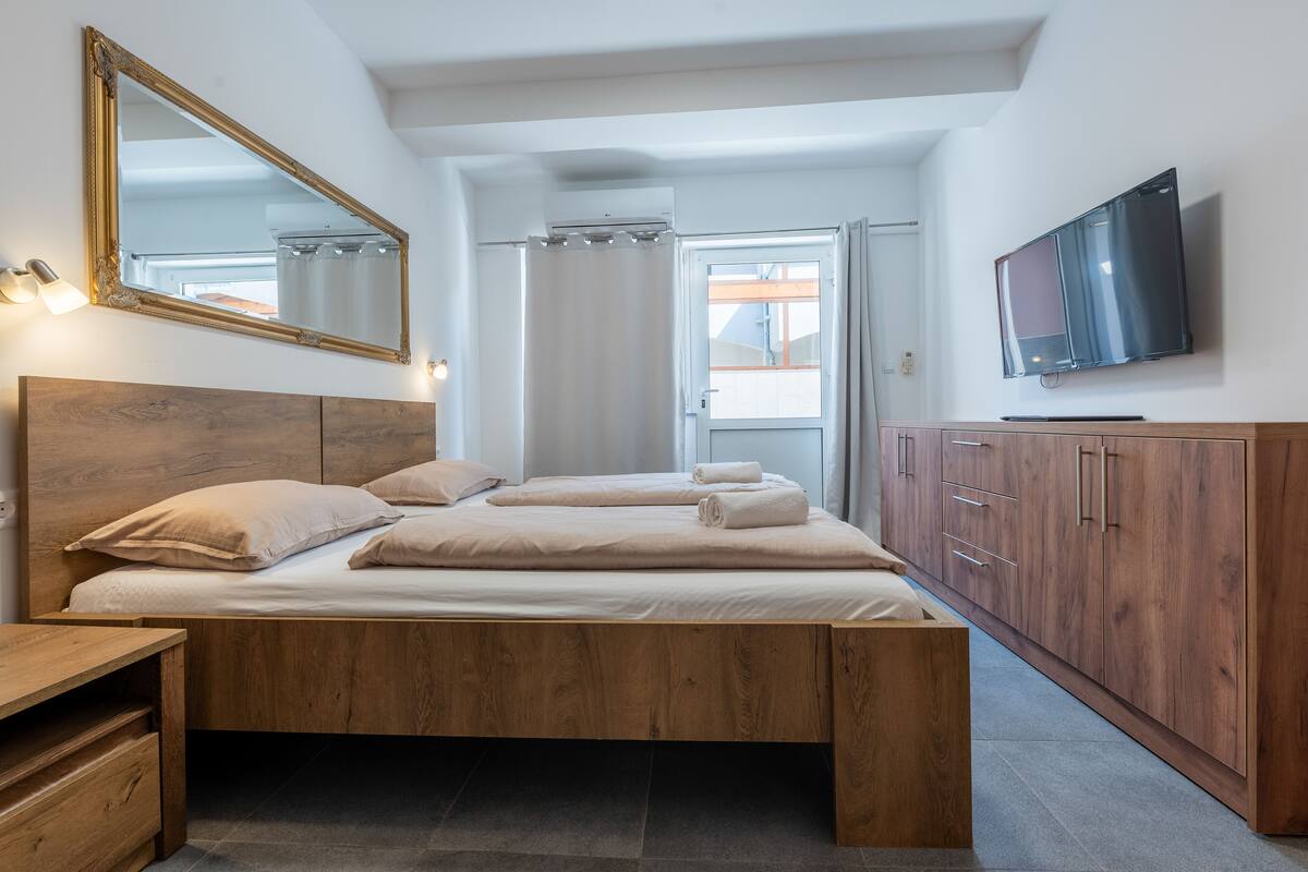 A bedroom with a wooden bed, a large mirror, a TV, and a wardrobe.