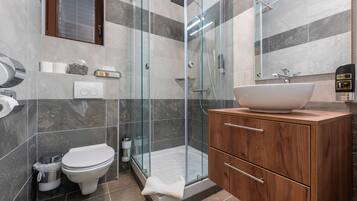 Un baño moderno con ducha de vidrio, tocador de madera con un lavamanos grande y un inodoro.