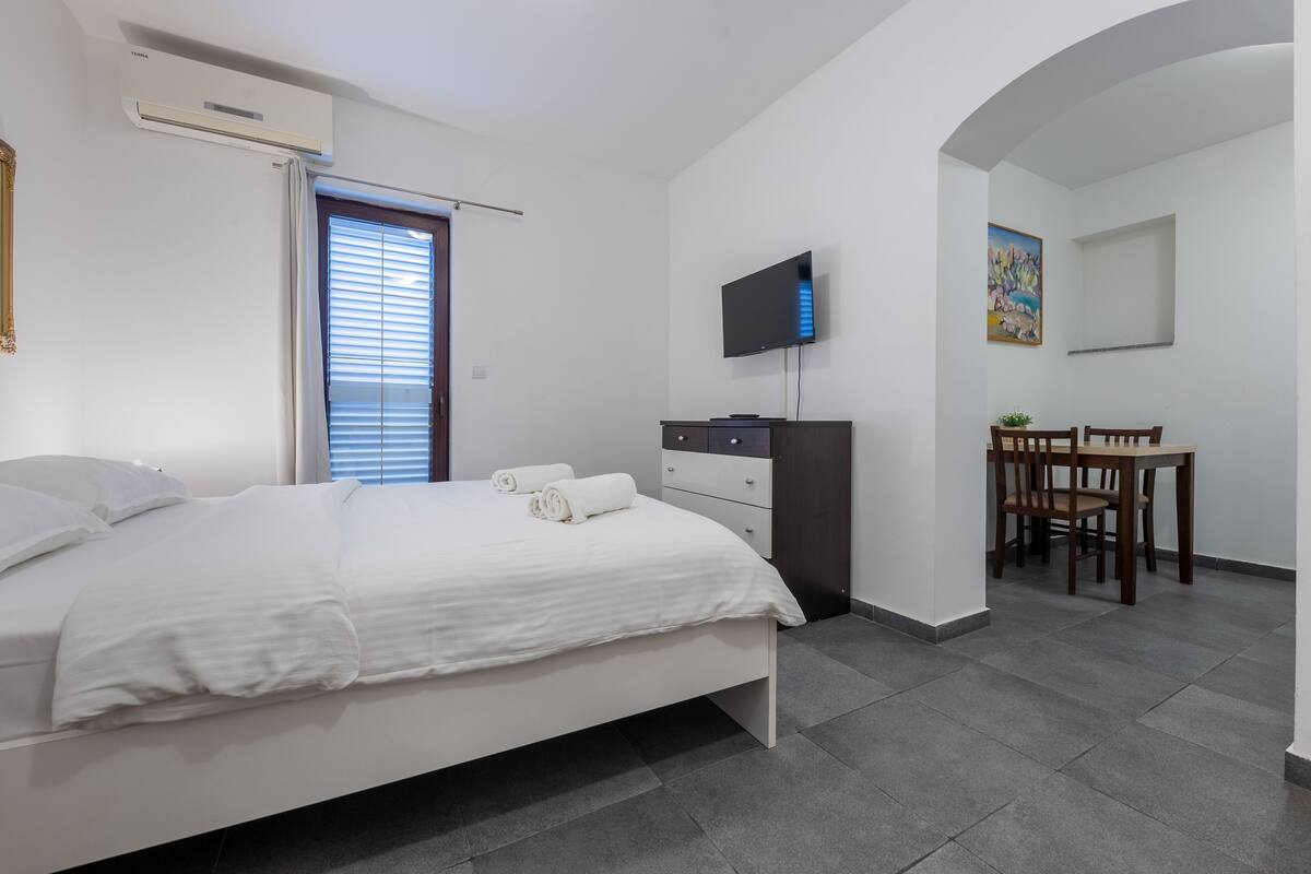 A modern bedroom with a bed, a TV, a desk, and a chair.