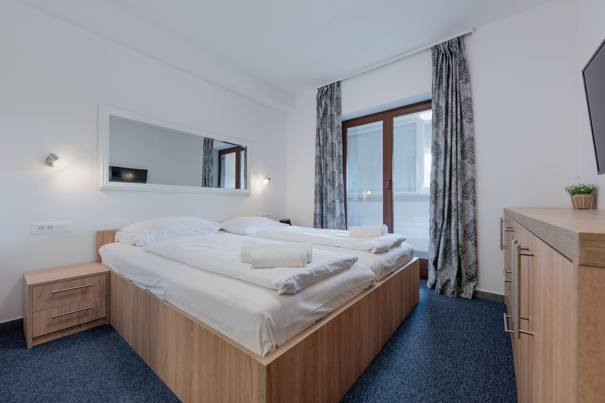 A bedroom with a large bed, a bedside table, a mirror, and a window with curtains.