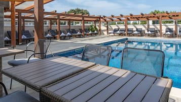 Un área junto a la piscina con sillones, mesas y una pérgola.