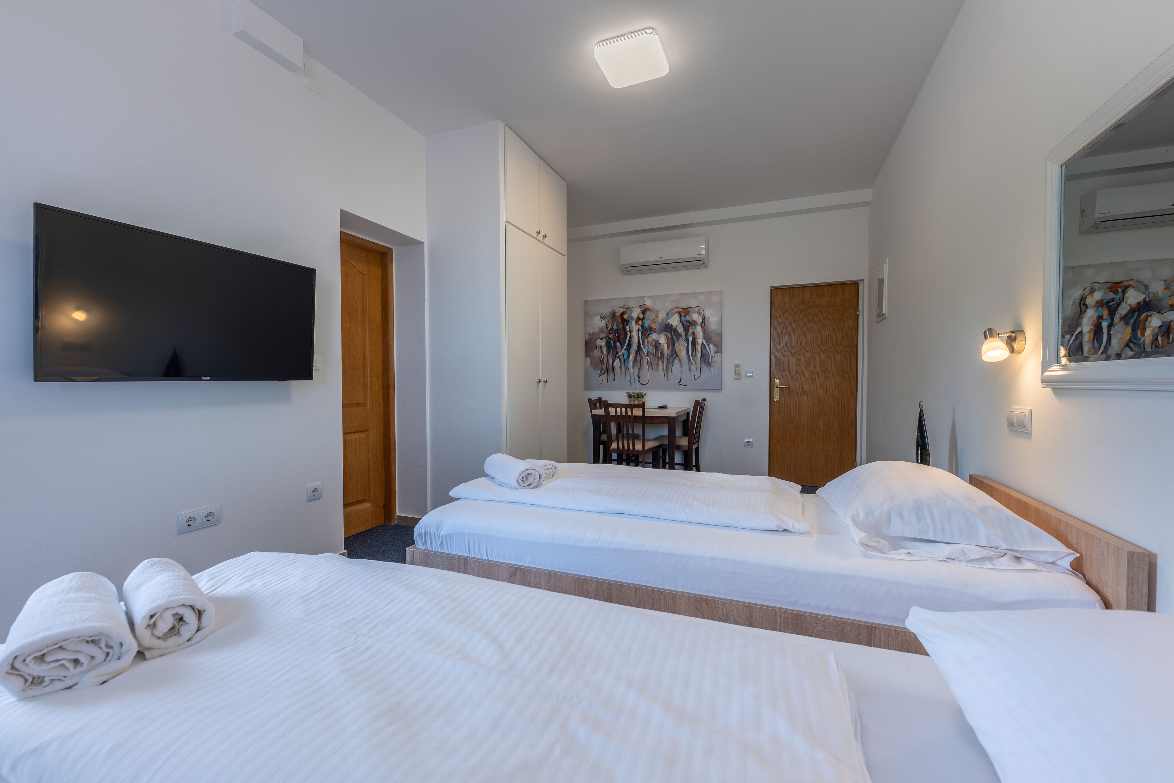 Een hotelkamer met twee bedden, een wandgemonteerde flatscreen-tv, een zithoek met een tafel en stoelen, en een airconditioner.