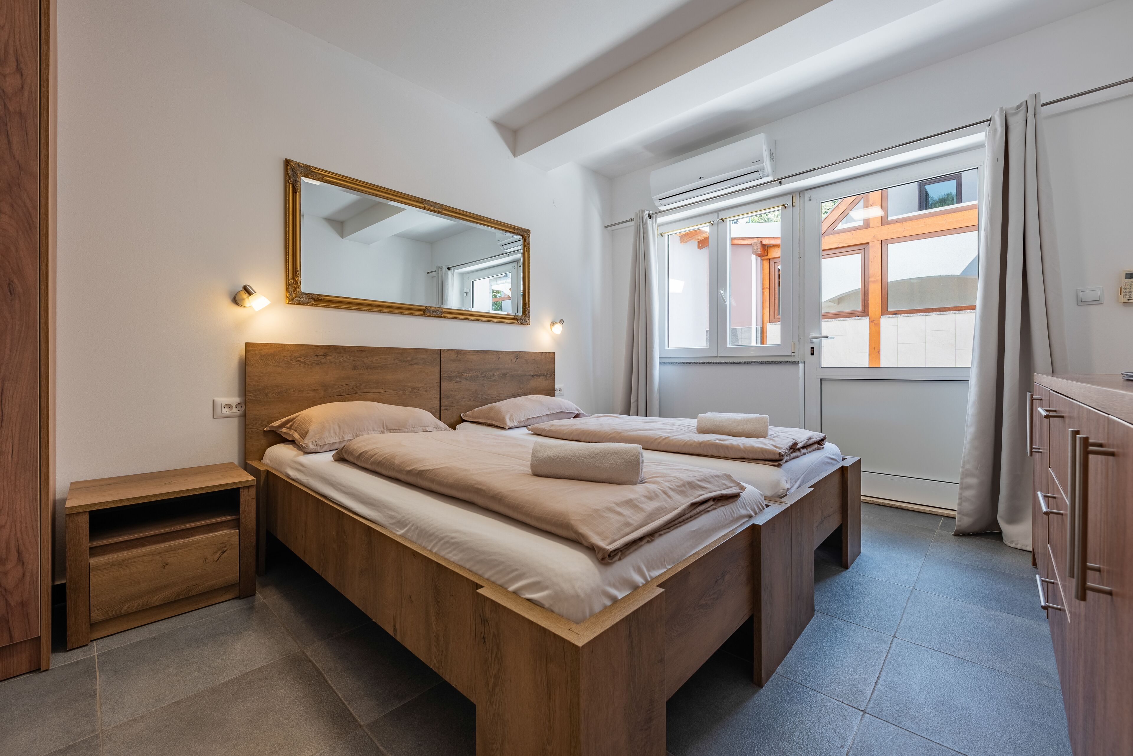 A bedroom with a wooden bed, a nightstand, a mirror, and a window with curtains.