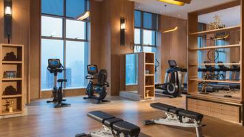 A modern gym with cardio machines, weight benches, and a large window offering a city view.