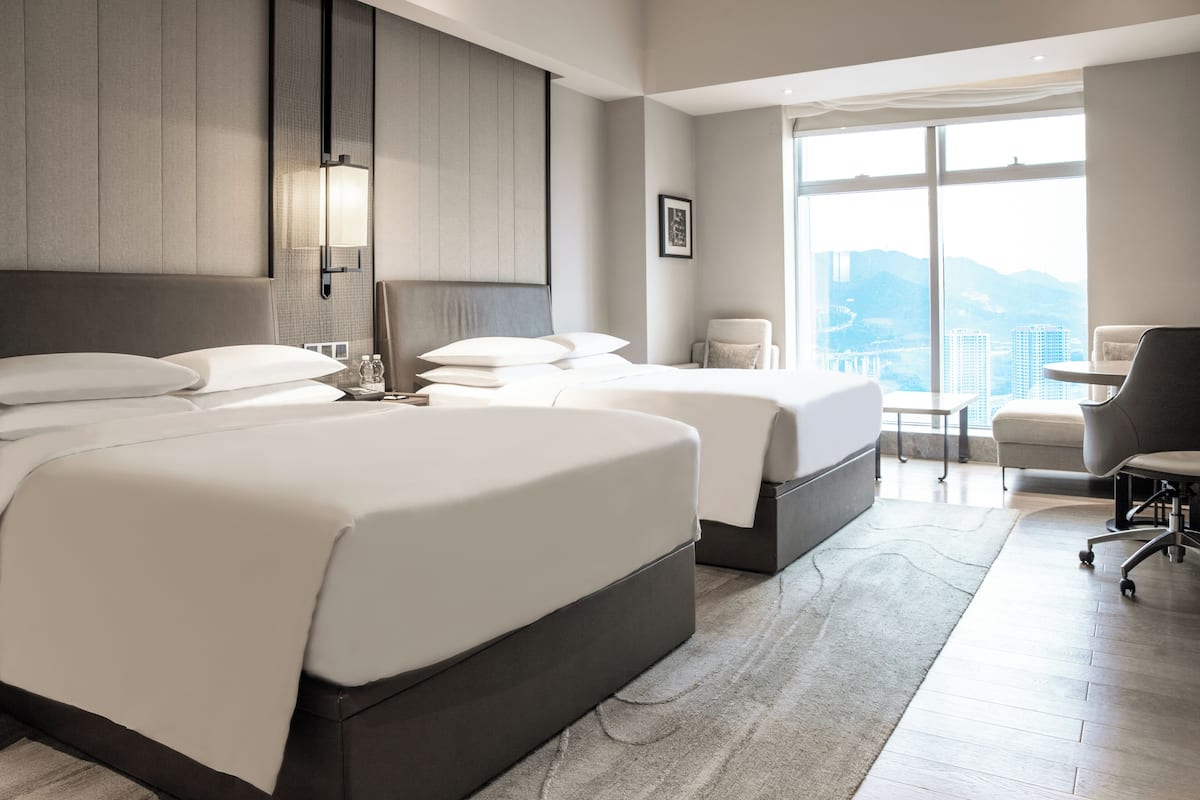 A modern hotel room with two beds, a desk, and a chair.