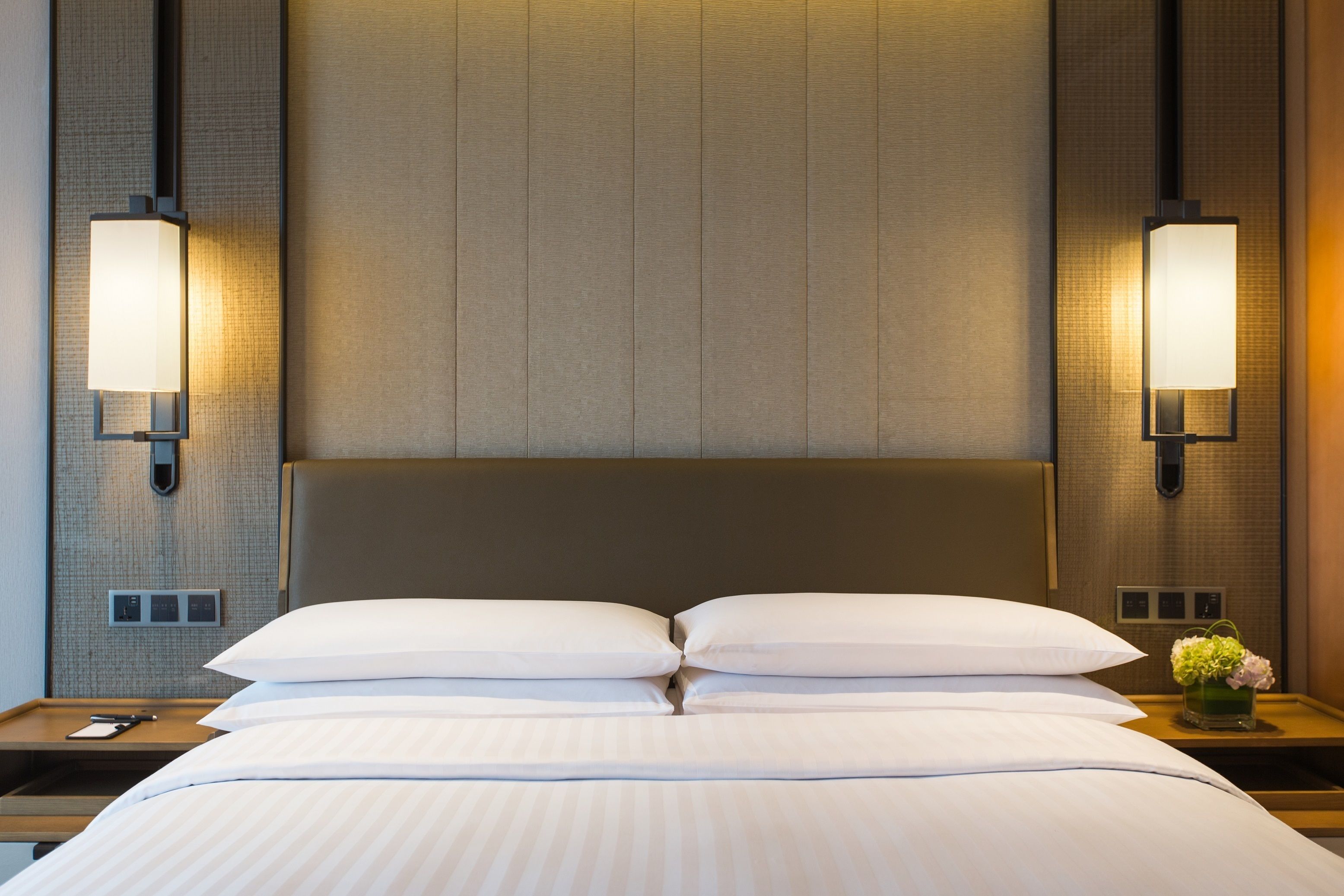 Une chambre d’hôtel avec un grand lit, deux tables de chevet et des lampes fixées au mur.