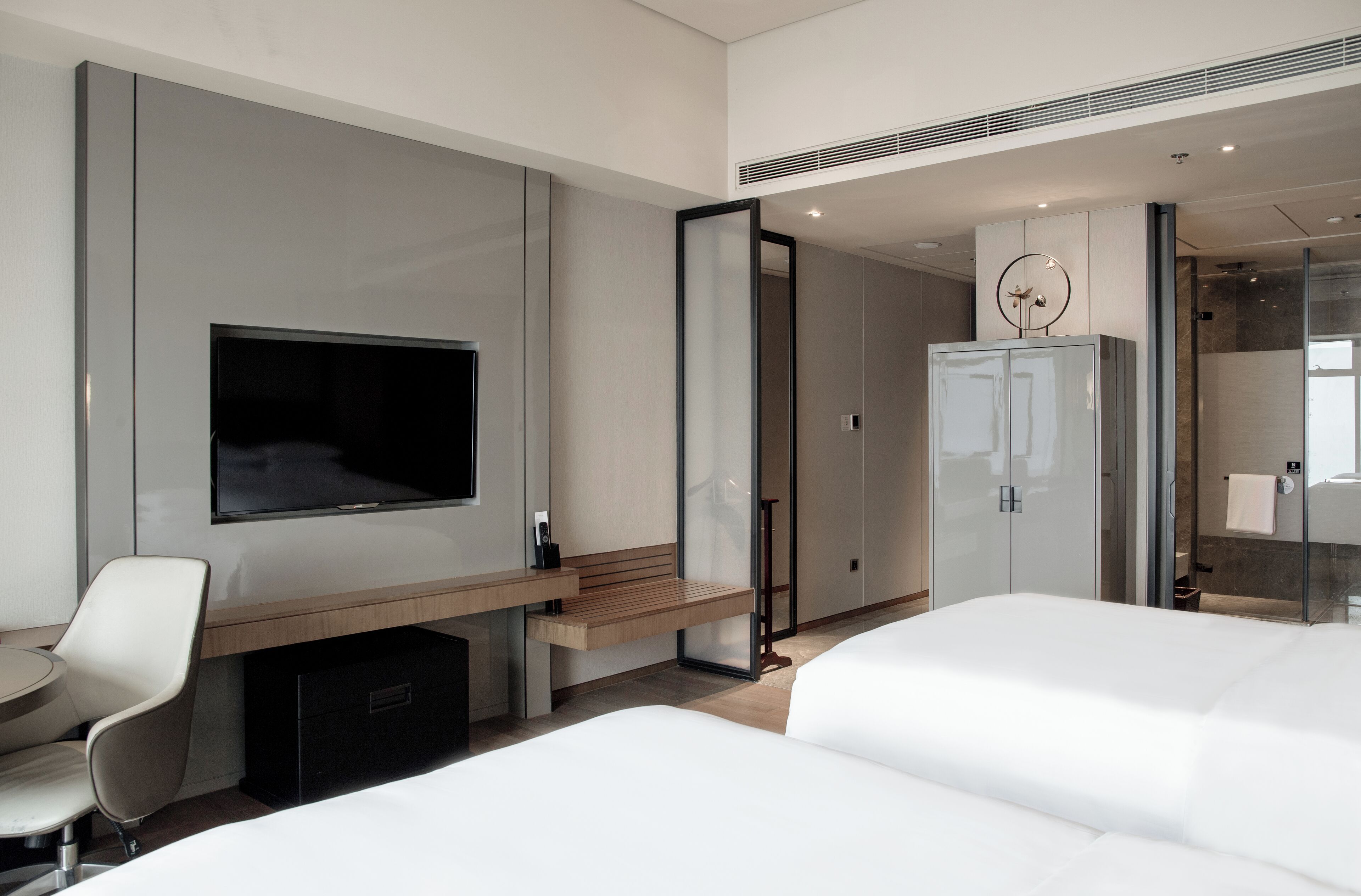 Una habitación de hotel moderna con una cama grande, un escritorio con silla, un televisor en la pared y un armario.