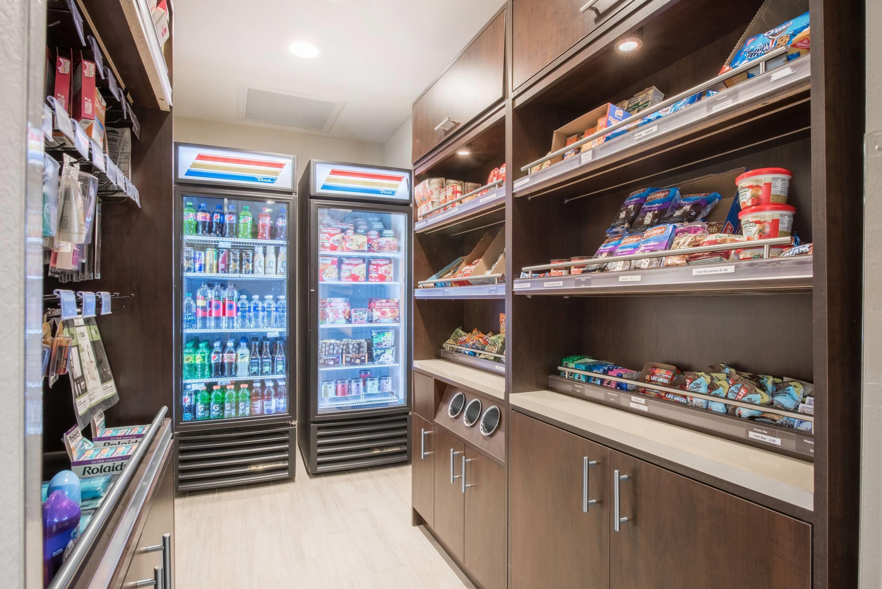 Una tienda de conveniencia con dispensadores de bebidas refrigeradas, estantes con bocadillos y una variedad de productos envasados.