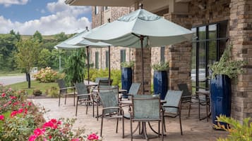 A patio with outdoor seating and umbrellas, a stone building with windows, and a view of the landscape.