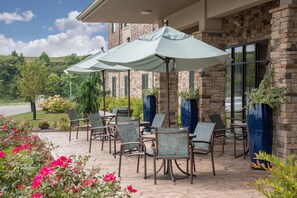 Eine Terrasse mit Sitzgelegenheiten und Sonnenschirmen, ein Gebäude aus Stein mit Fenstern und ein Blick auf die Landschaft.