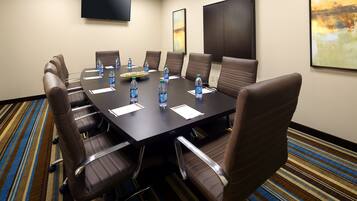 A conference room with a large table, brown leather chairs, water bottles, and a flat-screen TV on the wall.