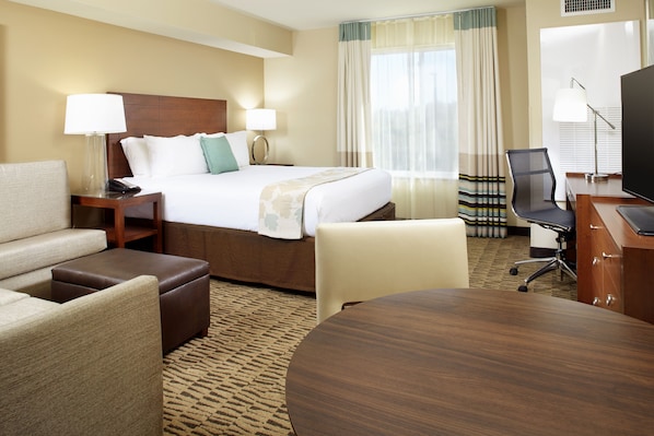 Habitación de hotel con cama, dos mesitas de noche con lámparas, un escritorio con silla, una mesa redonda y un televisor.