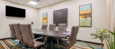 A conference room with a large table, six chairs, a flat-screen TV, two paintings, and a potted plant.