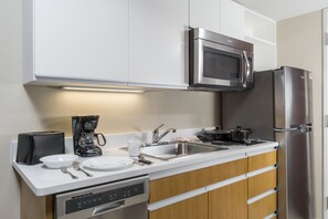 Una cocina moderna con armarios blancos, electrodomésticos de acero inoxidable, lavavajillas y cafetera.