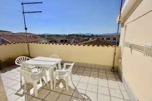 A balcony with a table and chairs, a TV antenna, and a view of buildings and mountains in the distance. - B&B Lucia (Olbia)