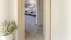 A hallway leading to a bedroom with a bed, a nightstand, and a potted plant. - B&B Lucia (Olbia)