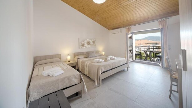 A bedroom with two beds, a wooden ceiling, and a balcony with a table and chairs. - B&B Lucia (Olbia)