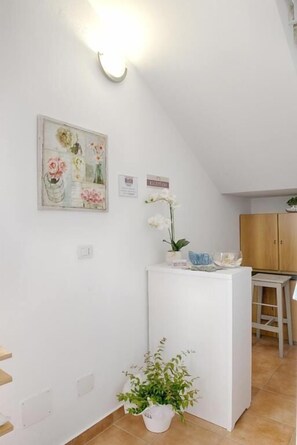 A white interior with a kitchen area, a white counter, and a potted plant. - B&B Lucia (Olbia)