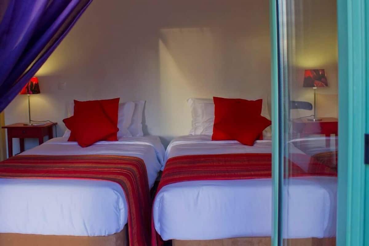 Quarto de hotel com duas camas, cada uma com roupa de cama vermelha e branca, e um separador de vidro.