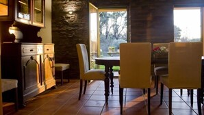 A dining area with a stone wall, a wooden cabinet, and a view of trees outside. - Vale de Ferreiros (Abrantes)